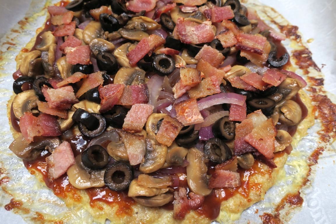 Chicken Crust BBQ pizza is topped with red onions, mushrooms, black olives, and bacon