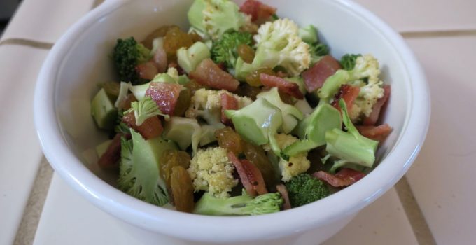 broccoli cauliflower bacon are mixed with golden raisins and vinegrette