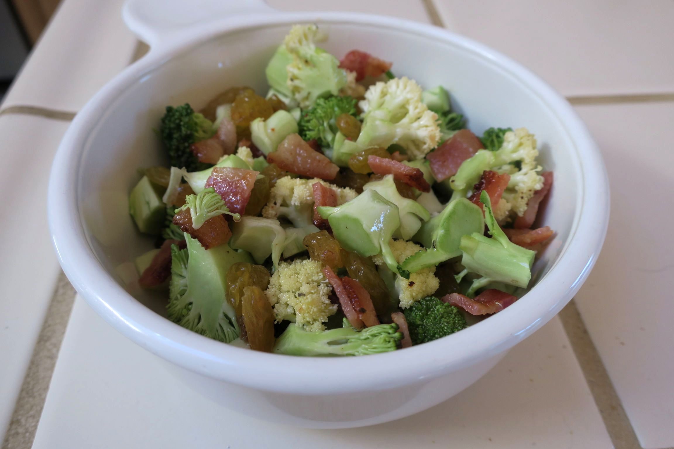 broccoli cauliflower bacon are mixed with golden raisins and vinegrette