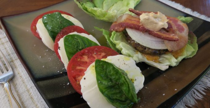 Caprese Salad - Tomato and basil with mozzarella next to a cheeseburger on lettuce leaves