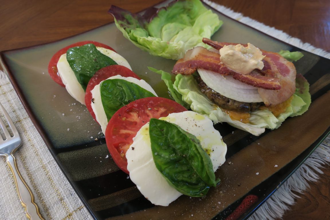 Caprese Salad - Tomato and basil with mozzarella next to a cheeseburger on lettuce leaves