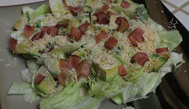 avocado bacon Caesar is iceberg lettuce topped with avocado, Caesar dressing, grated cheese, and bacon bits