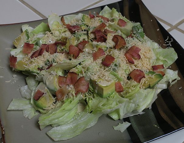 avocado bacon Caesar is iceberg lettuce topped with avocado, Caesar dressing, grated cheese, and bacon bits