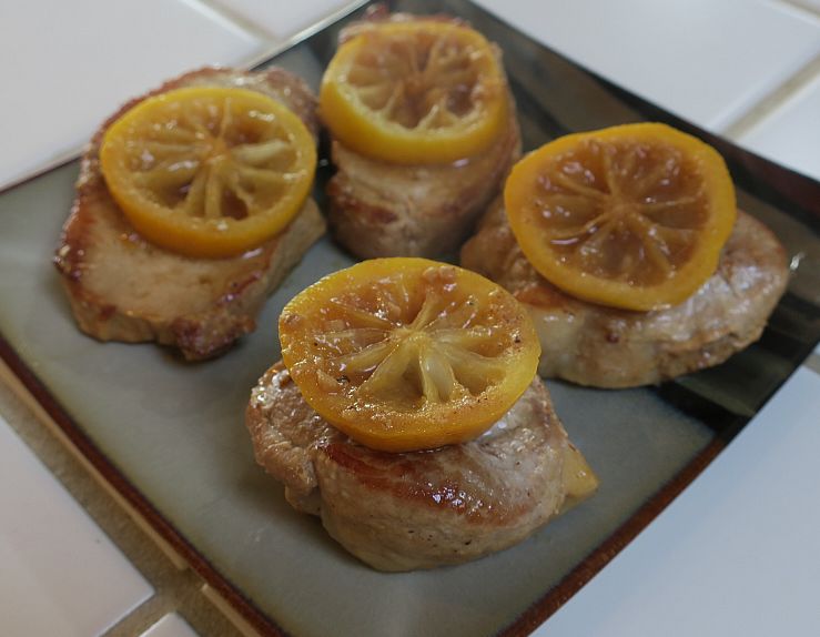 braised lemon pork chops topped with lemon slices on a plate