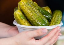 hands holding white bowl of dill pickles - a keto free food