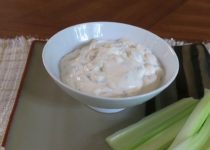 blue cheese dip in a white bowl on a tan plate with celery sticks