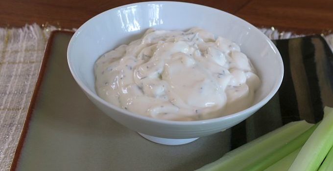 blue cheese dip in a white bowl on a tan plate with celery sticks
