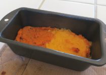 Savory sweet potato mash in a baking dish, one half covered in melted cheddar cheese