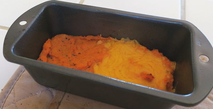 Savory sweet potato mash in a baking dish, one half covered in melted cheddar cheese